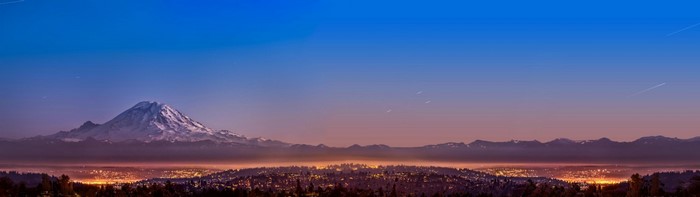 Snow-capped mountain overlooking a city at dusk