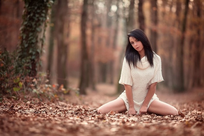 Woman in a white sweater sitting in an autumn forest