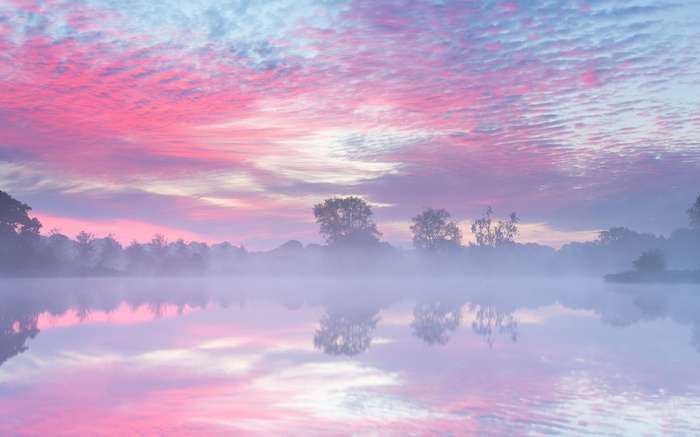 Pink and purple clouds over a misty lake at sunrise