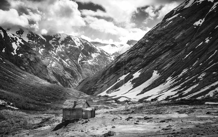 Monochrome landscape of a wooden cabin in a Norwegian valley with snow-capped mountains