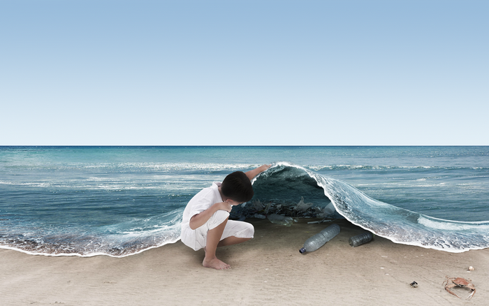 Boy looking at plastic bottles under a wave on a beach