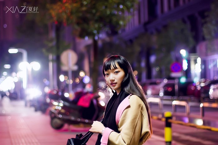Woman in coat at night with city lights