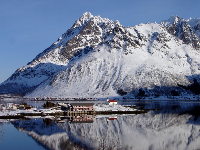 Snowy mountains reflected in a calm lake with a village