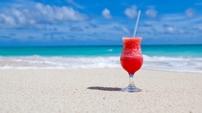 Red cocktail on a sandy beach with ocean background