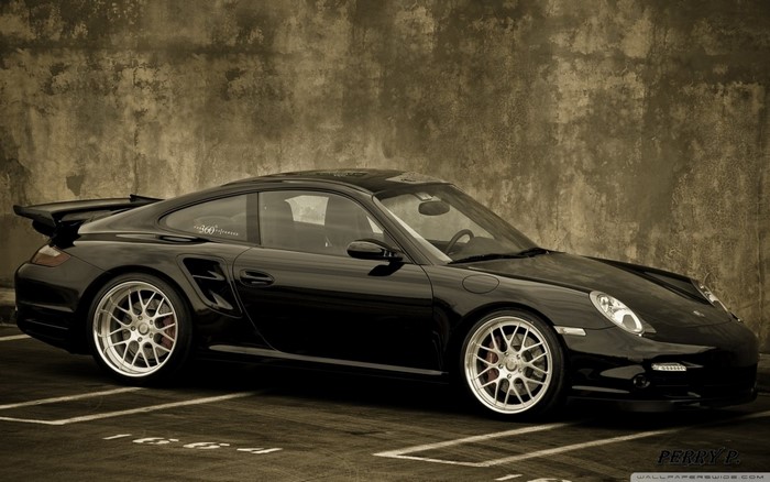 Black Porsche 911 sports car parked against a textured wall