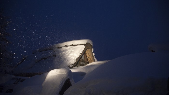 Snowy cabin roof at night with falling snow