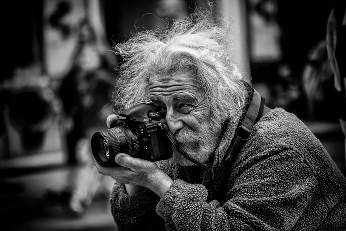 Elderly photographer with messy hair holding a Nikon camera