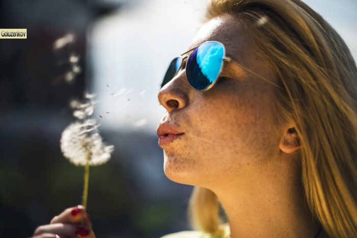 Woman blowing dandelion seeds wearing sunglasses