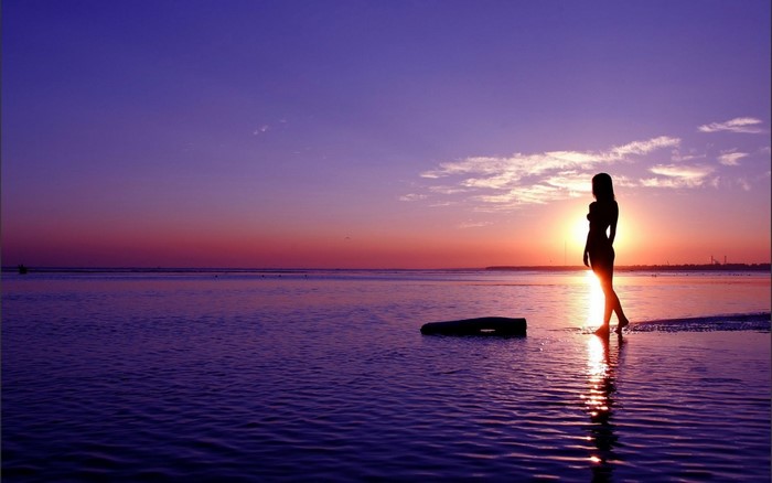Woman silhouetted against sunset over the sea