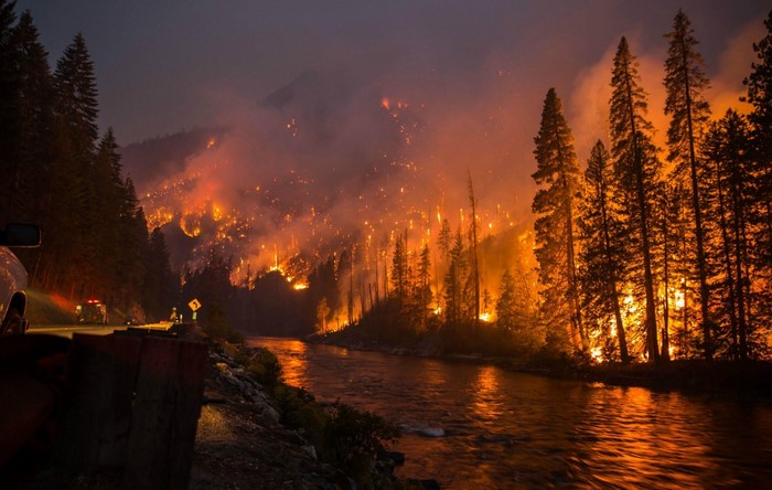 Wildfire raging on a mountainside at night with a river
