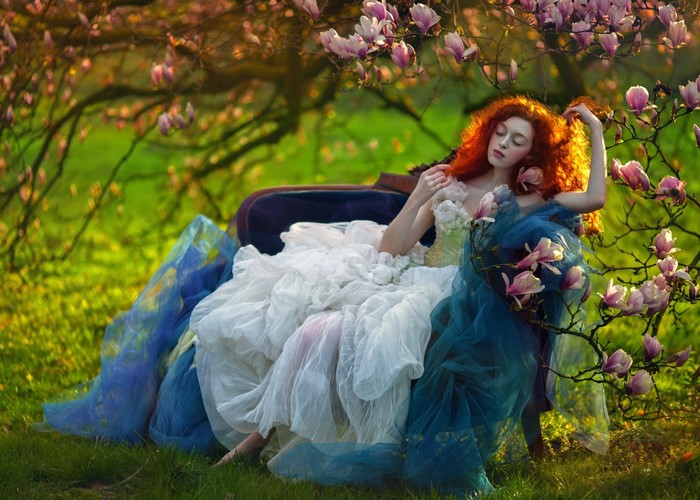 Woman with red hair in a white and blue dress sitting under a magnolia tree