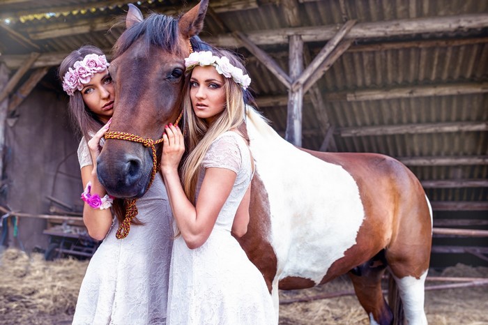 Two women with flower crowns and a horse in a barn