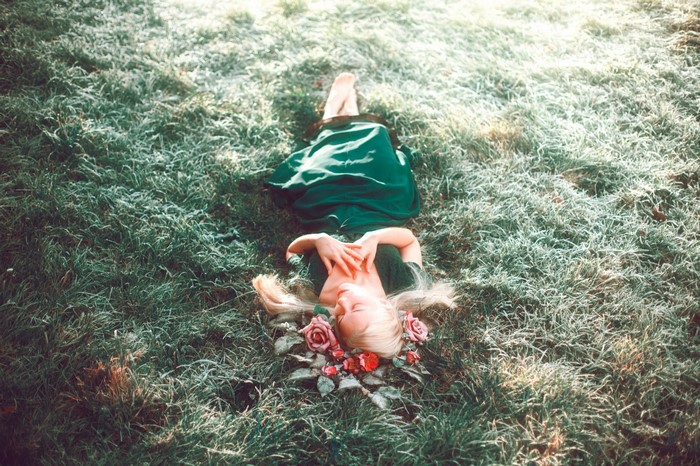 Woman in green dress lying on grass with flowers