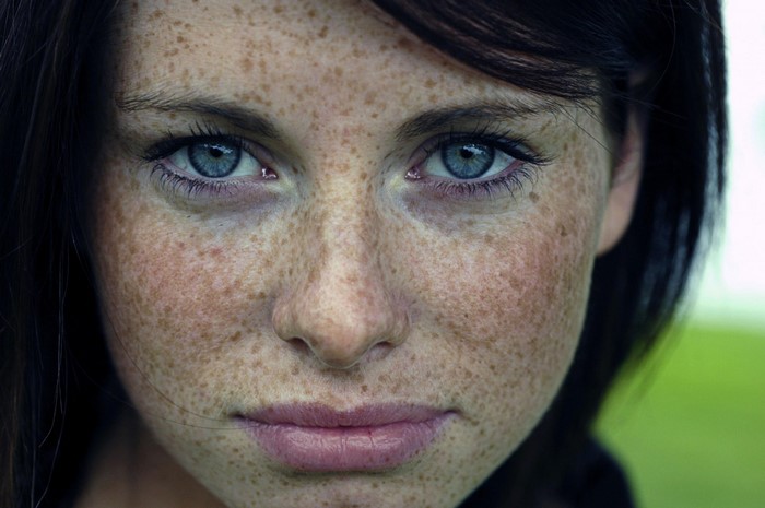 Close-up portrait of a young woman with freckles and blue eyes