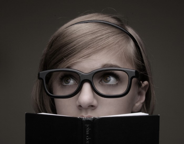 Close up of a young woman wearing glasses and reading a book