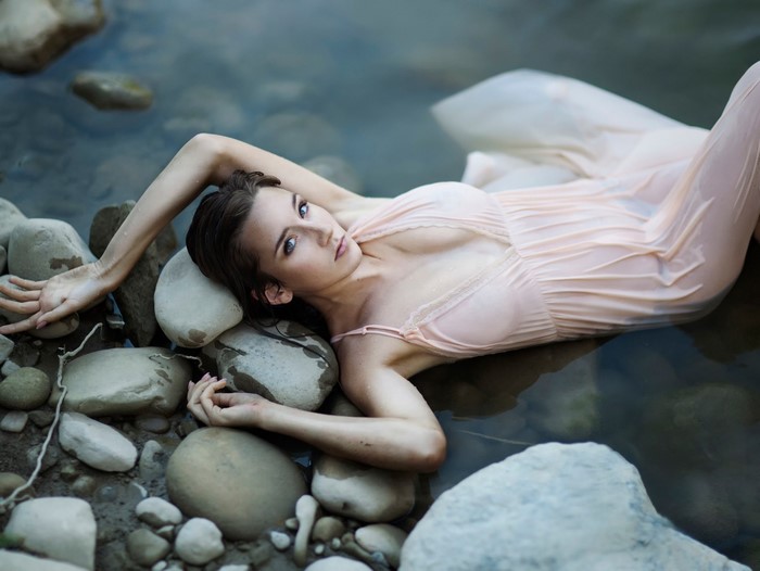 Woman in Pale Pink Dress Reclining on Rocks in Water