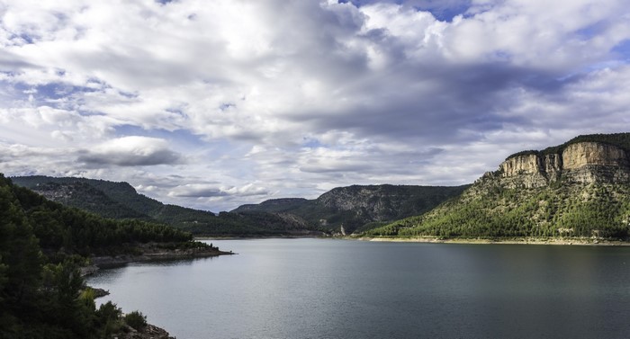 A vast lake surrounded by forested mountains under a cloudy sky