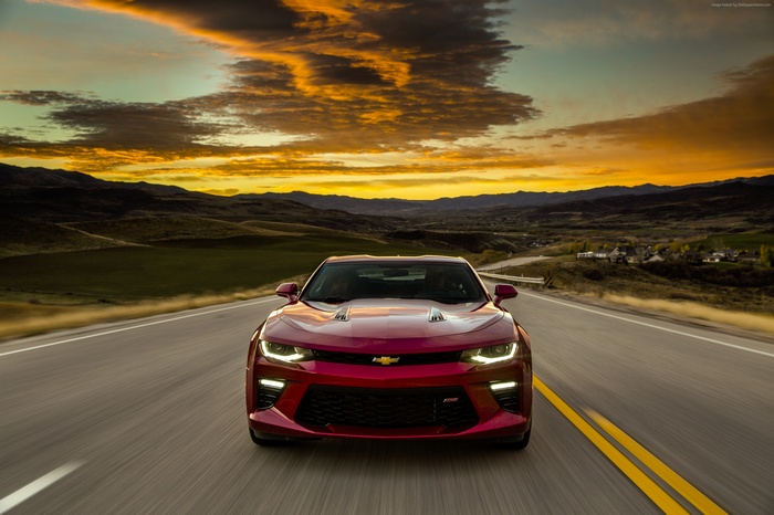 Red Chevrolet Camaro driving on a road at sunset