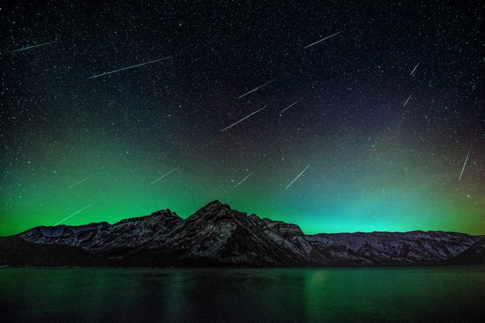 Meteor shower over mountains and lake at night