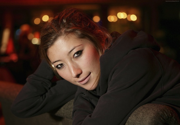 Dichen Lachman wearing a hoodie on a sofa