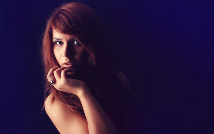 Redhead woman with hand on chin in dark portrait