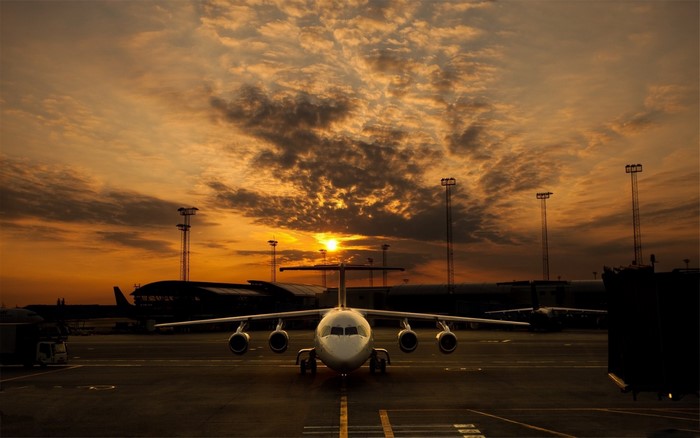 Airplane on tarmac at sunset with dramatic clouds