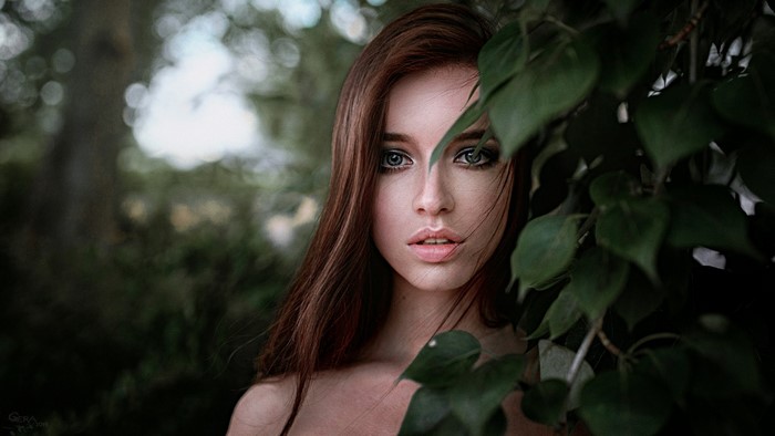 Woman with long brown hair peeking through leaves