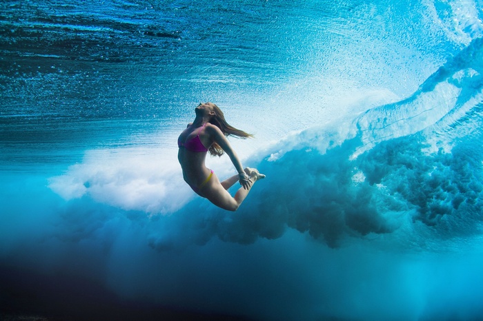 Girl underwater in a pink bikini surfing a wave