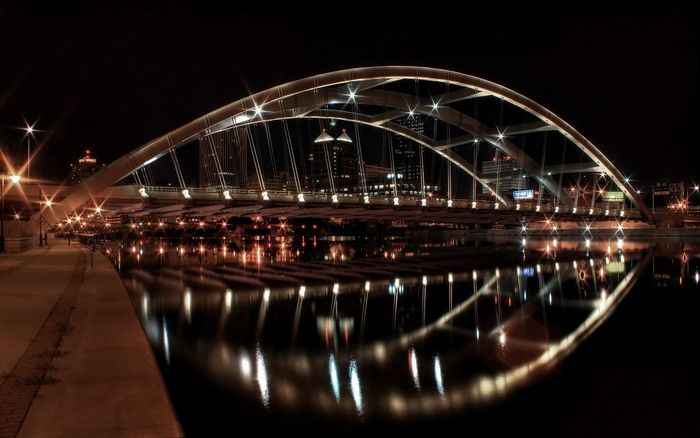 Illuminated bridge over water at night with city skyline