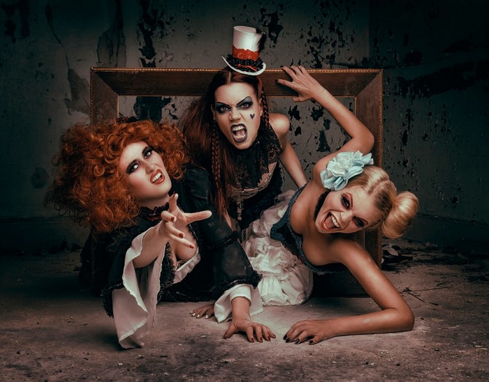 Three women in theatrical costumes in a derelict room