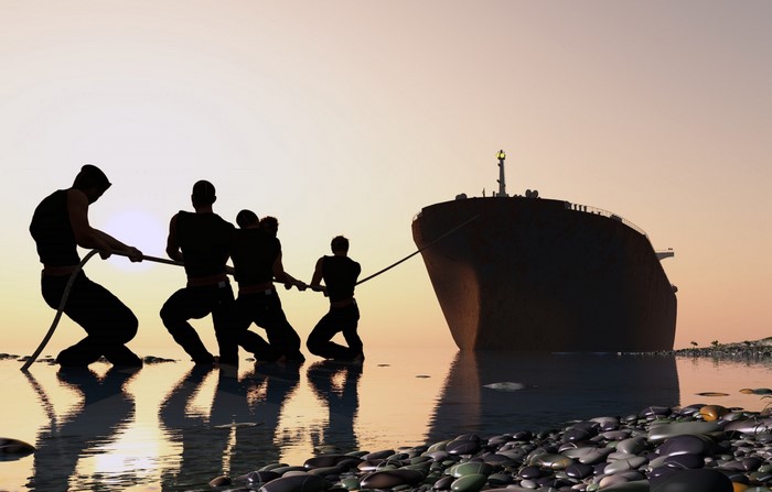 Silhouettes of men pulling a large ship at sunset