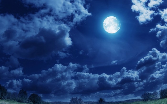 Full moon in a cloudy night sky over a landscape
