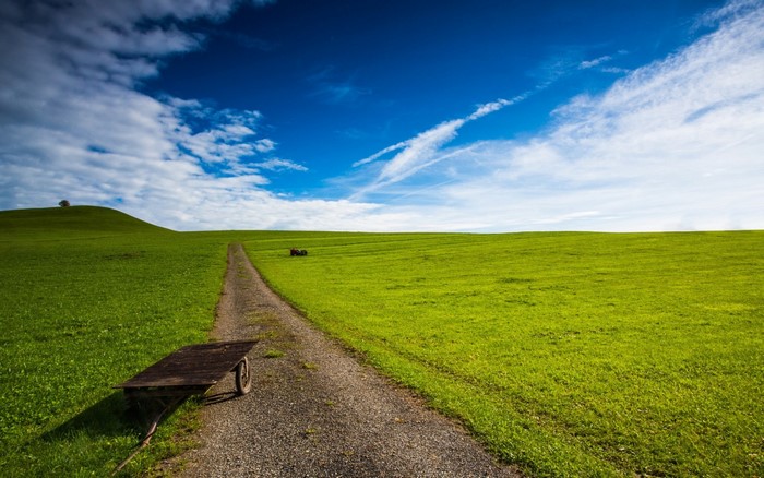 Dirt path through a green field with a cart and tractor