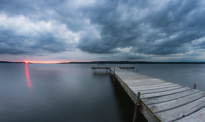 Wooden dock on a lake at sunset with stormy clouds