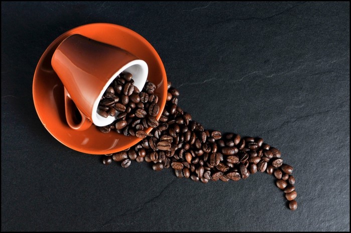 Orange coffee cup and saucer with spilled coffee beans