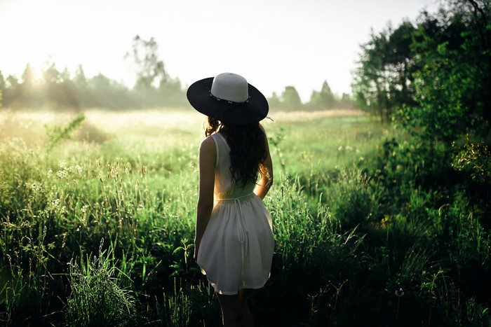 Woman in a white dress and hat in a grassy field at sunrise