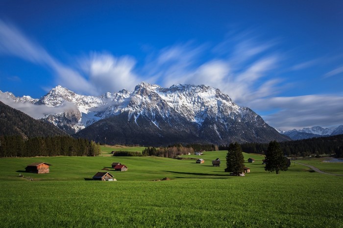 Snow-capped mountains over a green field with small cabins
