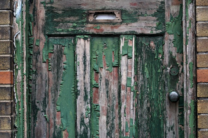 Peeling green paint on an old wooden door with a mail slot and doorknob