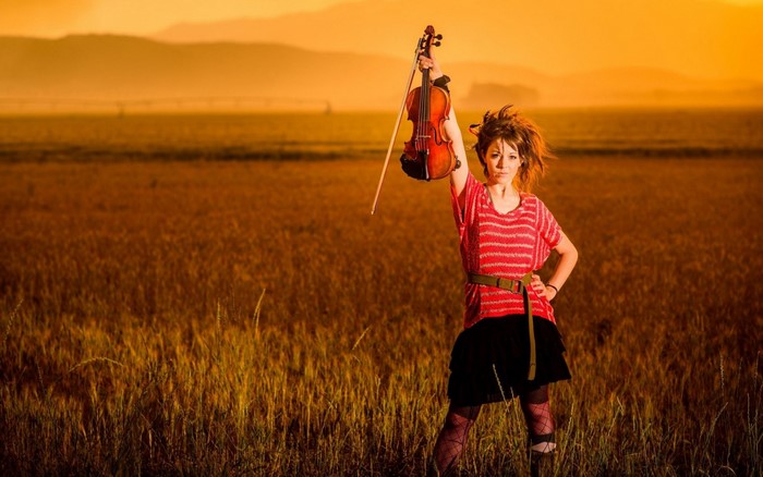 Lindsey Stirling with violin in a field at sunset