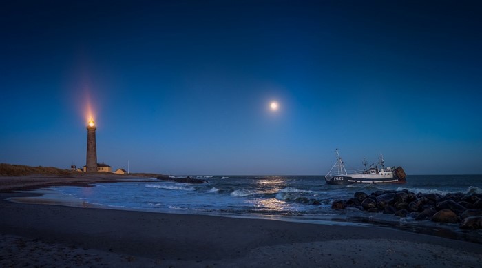 Lighthouse and ship at night with moon over the ocean