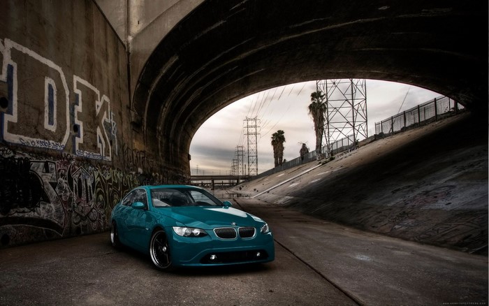 Teal BMW sports car parked under a bridge with graffiti
