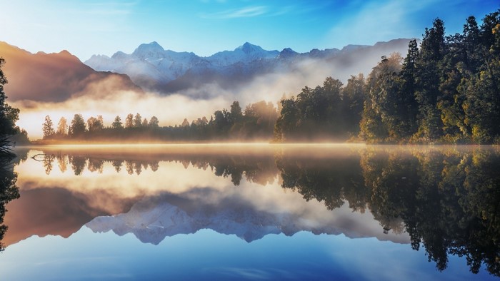 Misty lake reflection of mountains and forest at sunrise