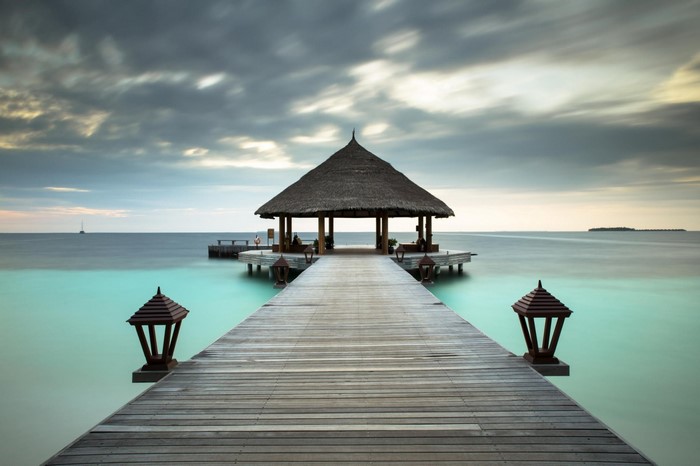 Wooden pier leading to a thatched-roof pavilion over turquoise water