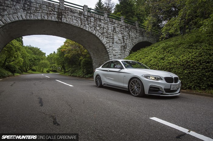 White BMW M235i driving under a stone bridge