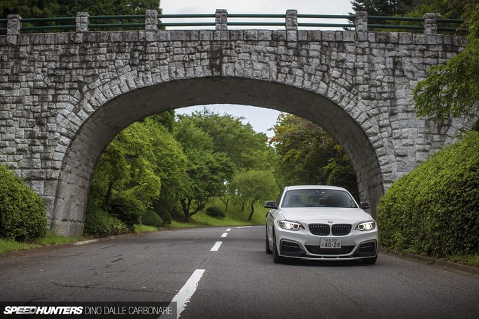 BMW M235i driving under a stone arch bridge