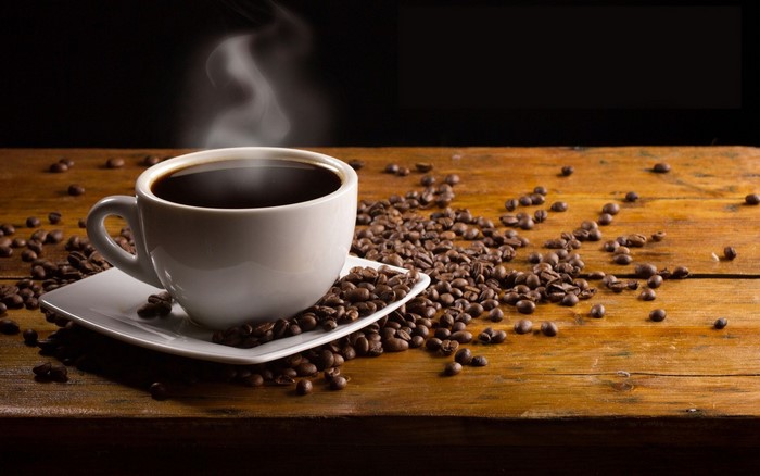 Steaming cup of coffee with beans on a wooden table