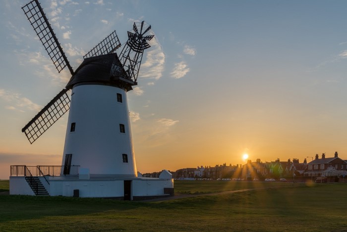 White windmill at sunset with coastal town