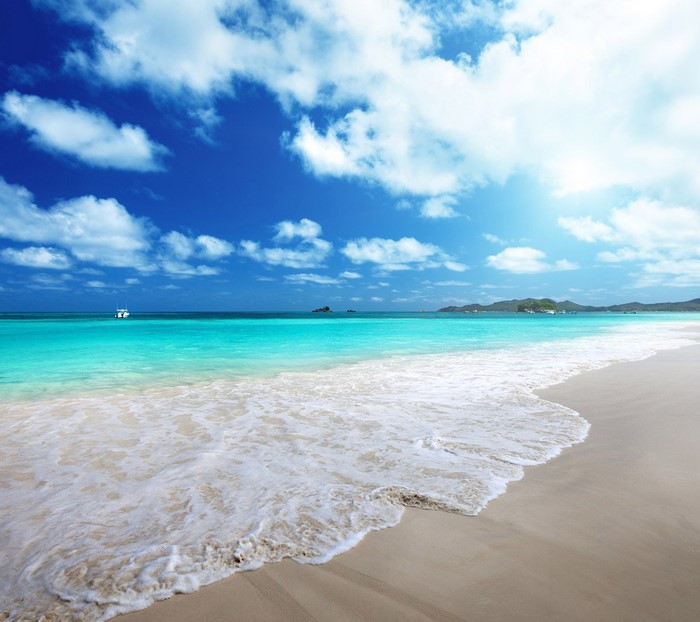 Turquoise ocean waves on a sandy beach under a blue sky with clouds