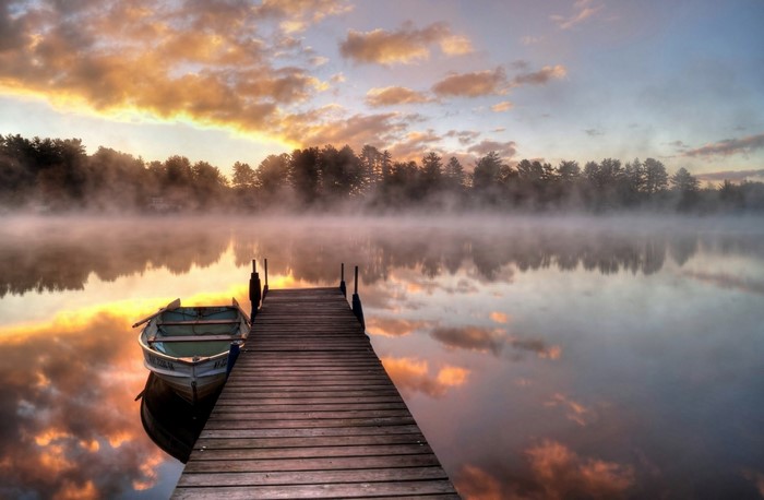 Wooden pier with a boat on a misty lake at sunrise