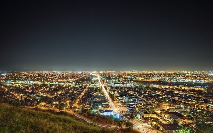 Cityscape at night with lights and a hill in the foreground